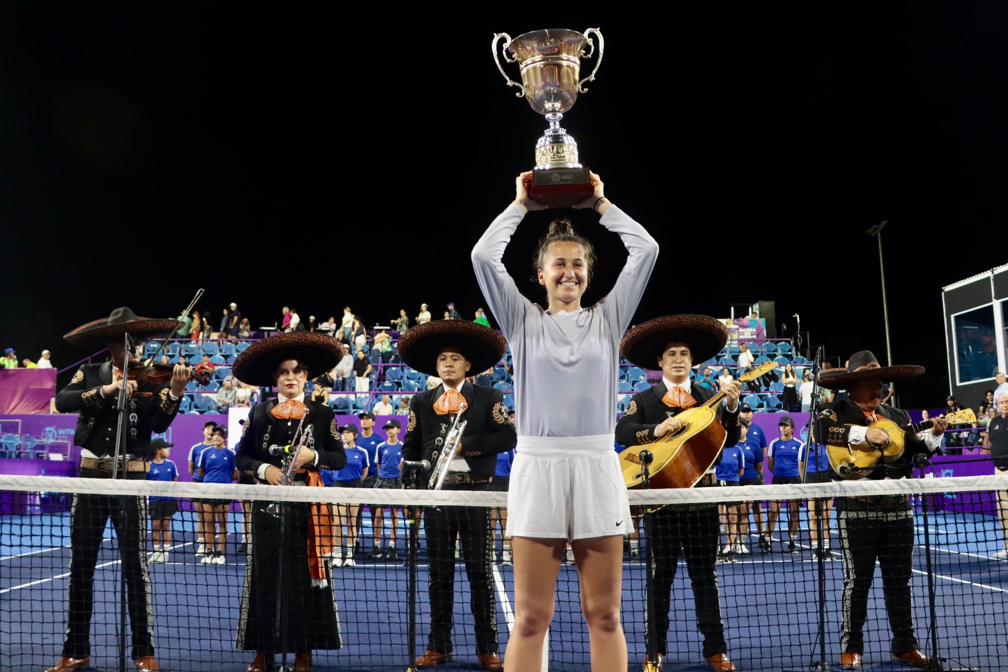Emina Bektas raises a trophy with a mariachi band playing behind her.